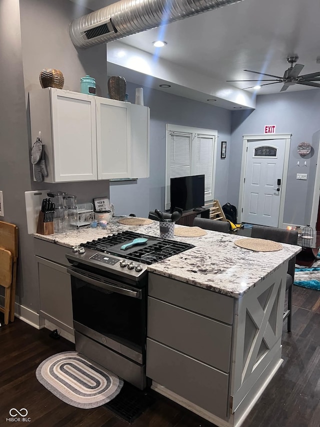 kitchen with light stone countertops, ceiling fan, dark wood-type flooring, stainless steel range with gas cooktop, and white cabinets