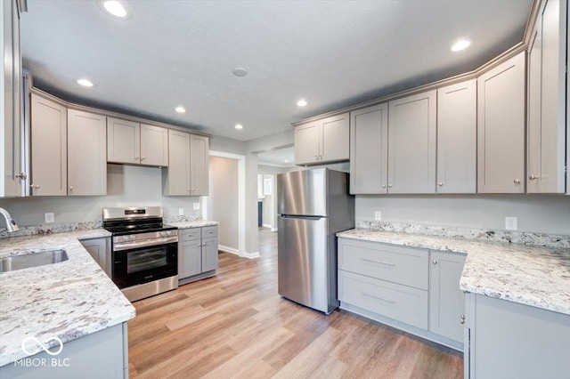 kitchen with stainless steel appliances, light wood finished floors, a sink, and gray cabinetry