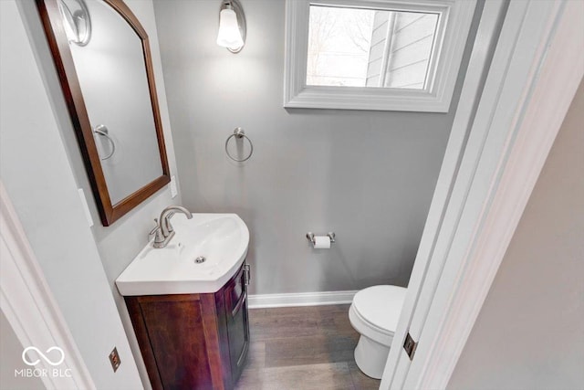 half bathroom with toilet, vanity, baseboards, and wood finished floors