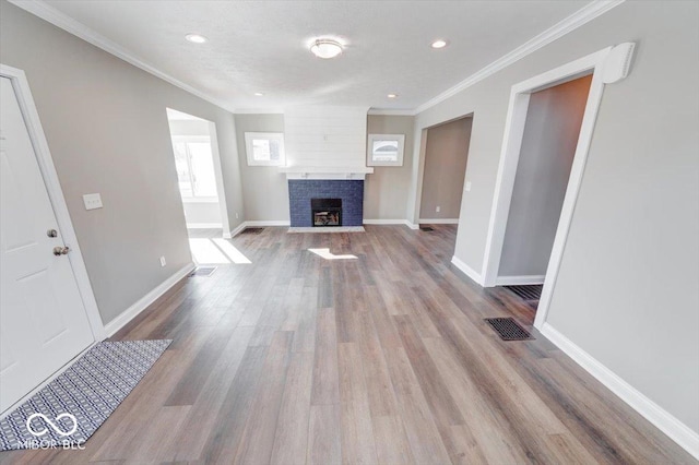 unfurnished living room with wood finished floors, a fireplace with flush hearth, visible vents, and crown molding