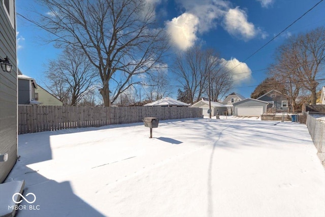 snowy yard featuring a detached garage and a fenced backyard