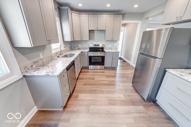 kitchen with stainless steel appliances, light stone counters, gray cabinets, and a sink