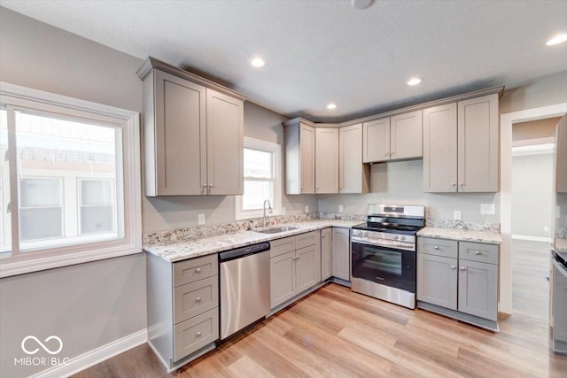 kitchen featuring appliances with stainless steel finishes, light wood-type flooring, a sink, and gray cabinetry