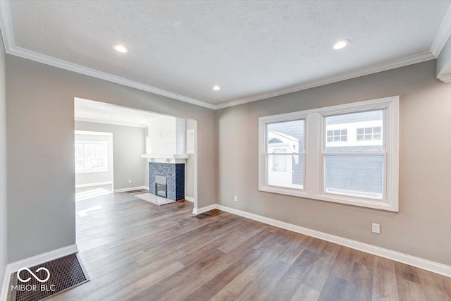 unfurnished living room featuring a textured ceiling, a fireplace with flush hearth, wood finished floors, baseboards, and ornamental molding