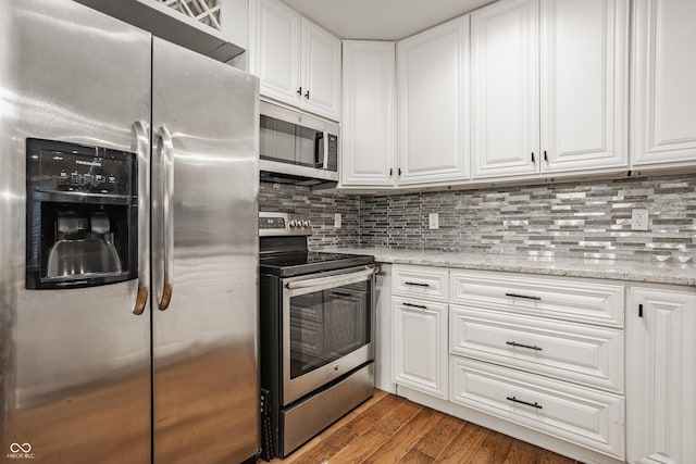 kitchen with hardwood / wood-style floors, decorative backsplash, appliances with stainless steel finishes, light stone counters, and white cabinetry