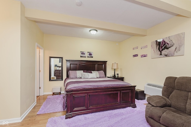 bedroom featuring beam ceiling, a wall unit AC, and light wood-type flooring