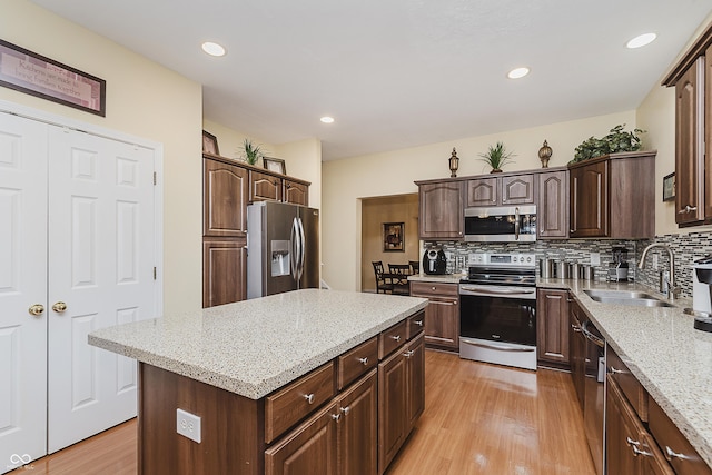 kitchen with decorative backsplash, light stone countertops, stainless steel appliances, light hardwood / wood-style floors, and a kitchen island