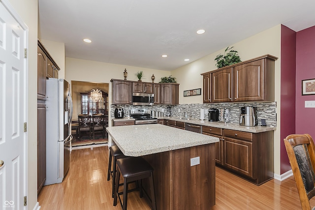 kitchen featuring light wood-type flooring, appliances with stainless steel finishes, tasteful backsplash, dark brown cabinets, and a kitchen island