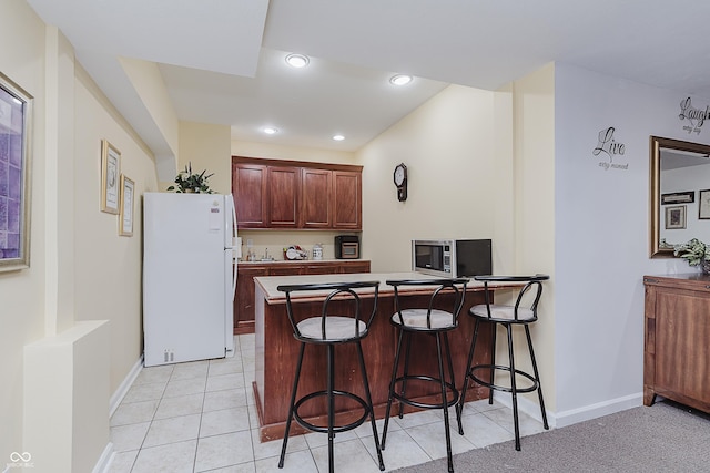 kitchen with a breakfast bar area, kitchen peninsula, light tile patterned flooring, and white refrigerator