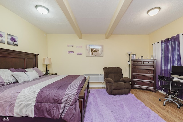 bedroom with beamed ceiling, a textured ceiling, light wood-type flooring, and a wall unit AC