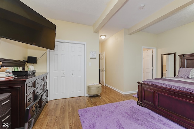 bedroom featuring beam ceiling, light wood-type flooring, and a closet