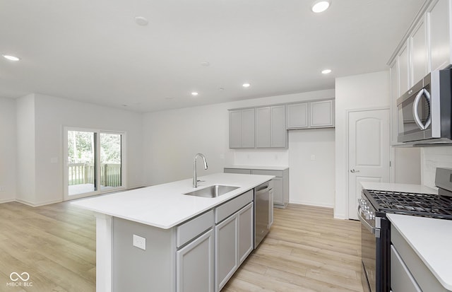 kitchen featuring a kitchen island with sink, appliances with stainless steel finishes, gray cabinetry, light wood-type flooring, and sink