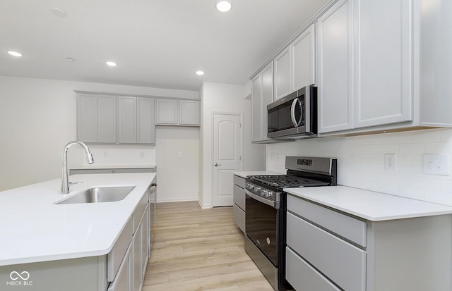 kitchen with stainless steel appliances, an island with sink, light hardwood / wood-style floors, gray cabinets, and sink