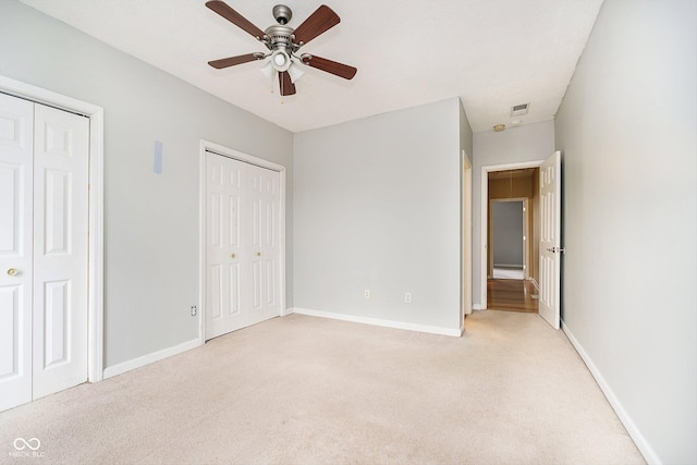 unfurnished bedroom featuring multiple closets, ceiling fan, and light carpet