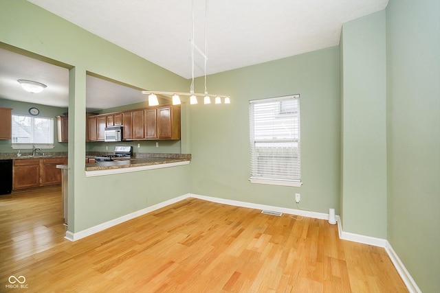 kitchen with kitchen peninsula, sink, black appliances, decorative light fixtures, and light hardwood / wood-style floors