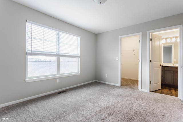 unfurnished bedroom featuring connected bathroom, a spacious closet, a closet, and carpet floors