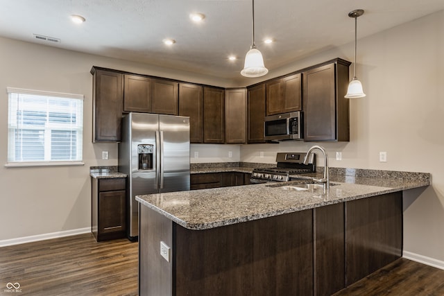 kitchen featuring kitchen peninsula, appliances with stainless steel finishes, light stone counters, dark brown cabinetry, and decorative light fixtures