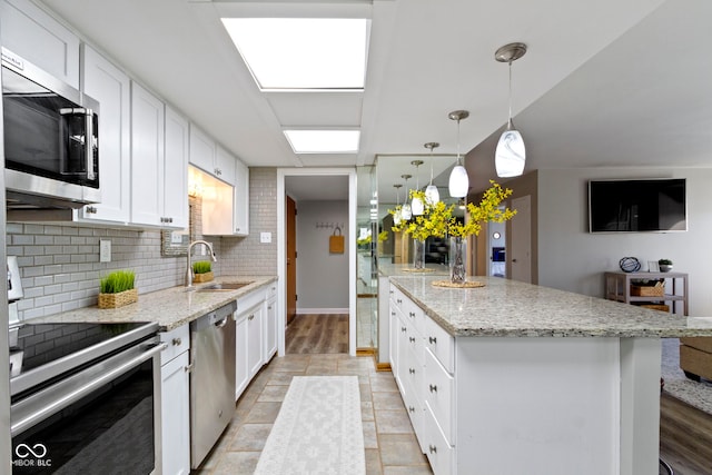 kitchen with hanging light fixtures, appliances with stainless steel finishes, sink, white cabinets, and a kitchen island