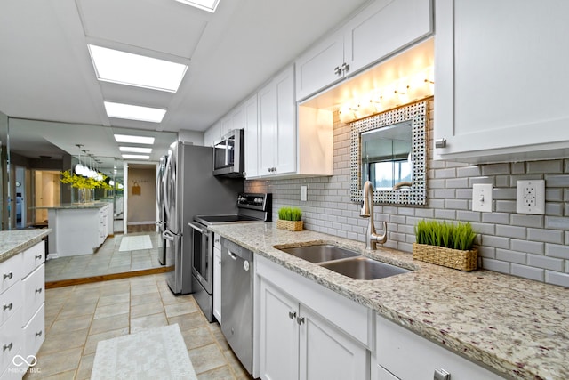 kitchen featuring white cabinetry, sink, backsplash, stainless steel appliances, and light stone counters