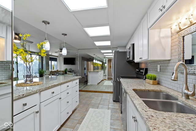 kitchen with sink, white cabinetry, light stone countertops, and hanging light fixtures