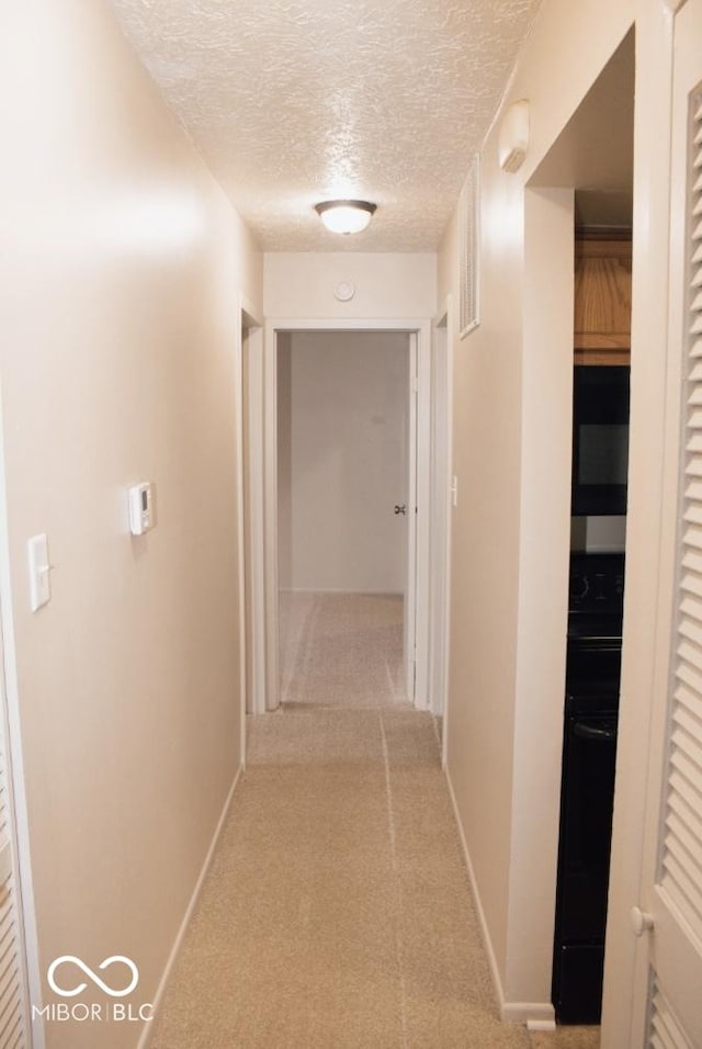 hall with a textured ceiling and light colored carpet