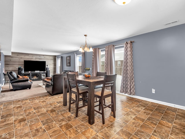 dining room featuring a notable chandelier, wood walls, and a fireplace