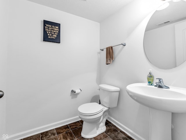 bathroom with a textured ceiling, toilet, and sink