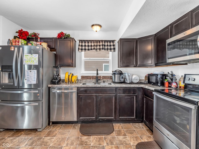 kitchen with sink, stainless steel appliances, dark brown cabinets, and stone countertops