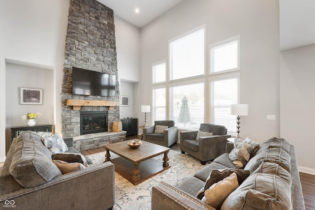 living room featuring a towering ceiling, a stone fireplace, and light wood-type flooring