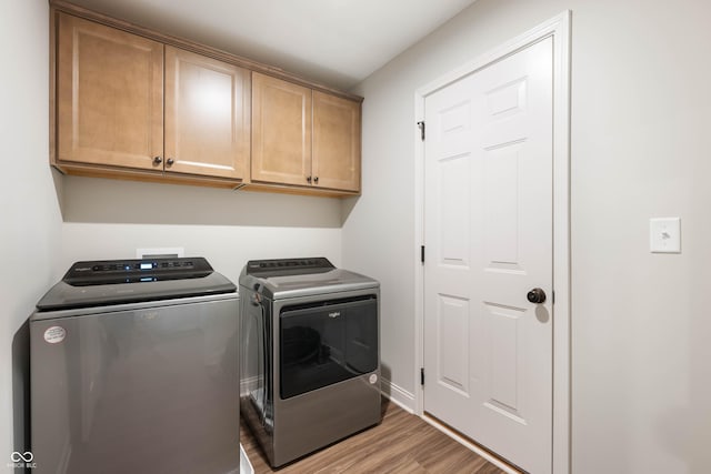 laundry room featuring light wood-type flooring, washing machine and clothes dryer, and cabinets