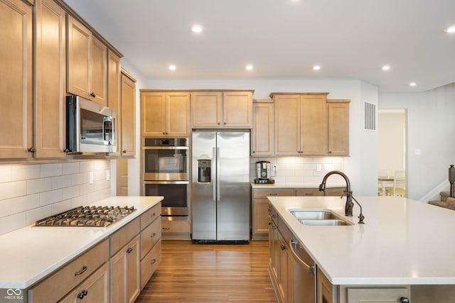 kitchen with decorative backsplash, appliances with stainless steel finishes, sink, and a center island with sink