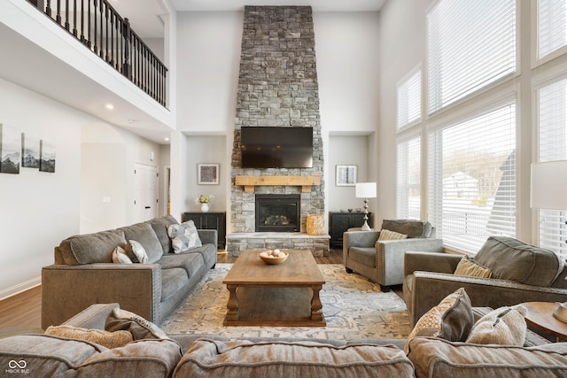 living room with light hardwood / wood-style floors, a towering ceiling, and a stone fireplace