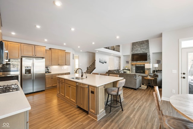 kitchen featuring hardwood / wood-style flooring, a center island with sink, a stone fireplace, appliances with stainless steel finishes, and sink