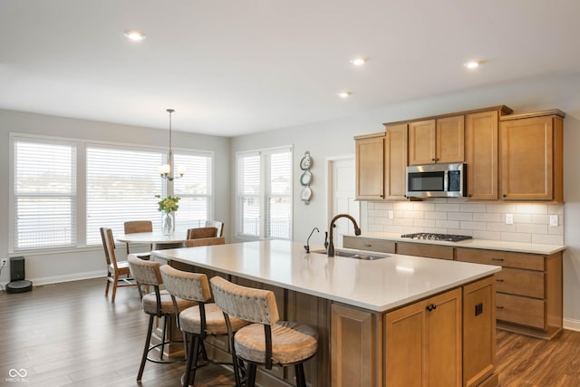 kitchen featuring stainless steel appliances, tasteful backsplash, a kitchen island with sink, hanging light fixtures, and sink