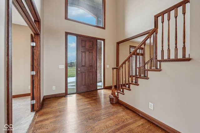 foyer entrance featuring stairs, wood finished floors, a towering ceiling, and baseboards