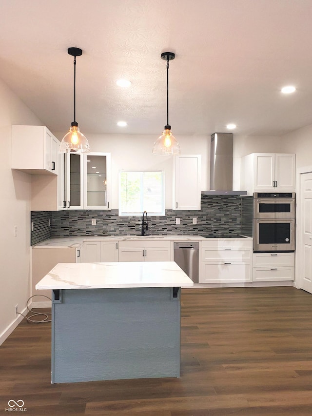 kitchen with white cabinets, pendant lighting, stainless steel appliances, and wall chimney range hood