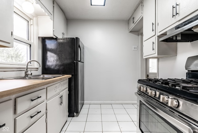 kitchen featuring black fridge, sink, white cabinets, stainless steel range with gas stovetop, and light tile patterned flooring