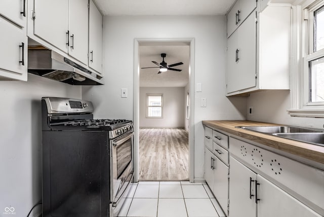 kitchen with ceiling fan, stainless steel gas stove, sink, light tile patterned floors, and white cabinets