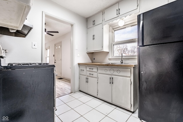 kitchen featuring ceiling fan, light tile patterned floors, black refrigerator, white cabinets, and range