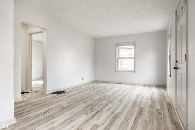 empty room with light wood-type flooring and a textured ceiling