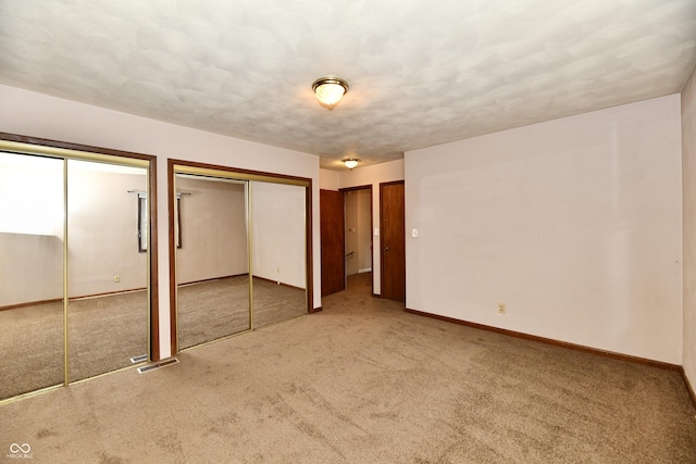 unfurnished bedroom featuring two closets and light colored carpet