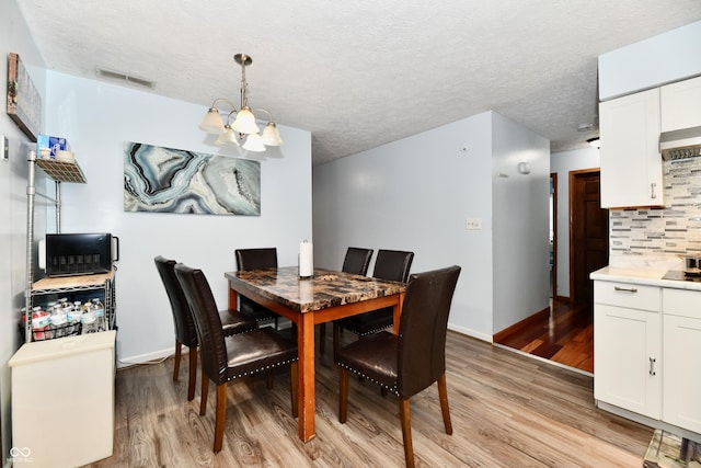 dining space with a textured ceiling, light hardwood / wood-style floors, and an inviting chandelier