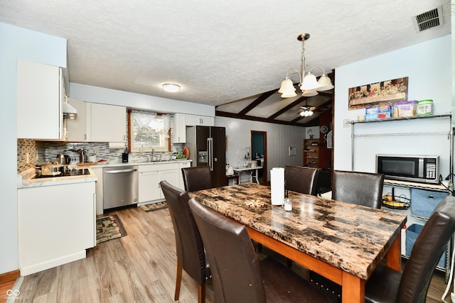 dining space with a textured ceiling, ceiling fan with notable chandelier, sink, light hardwood / wood-style flooring, and lofted ceiling