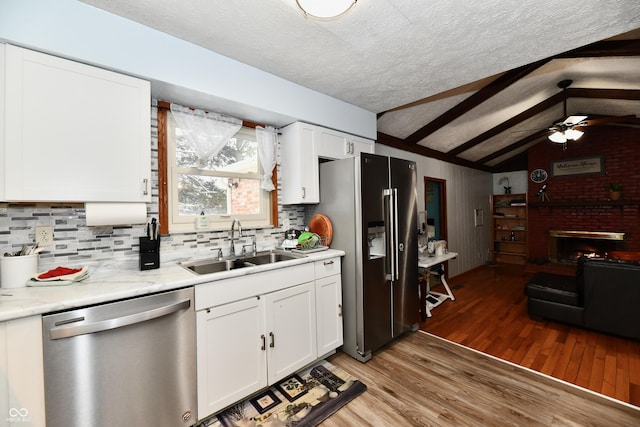 kitchen featuring appliances with stainless steel finishes, sink, wood-type flooring, lofted ceiling with beams, and white cabinetry