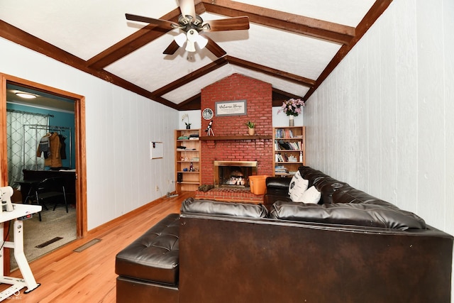 living room featuring vaulted ceiling with beams, ceiling fan, hardwood / wood-style floors, and a brick fireplace