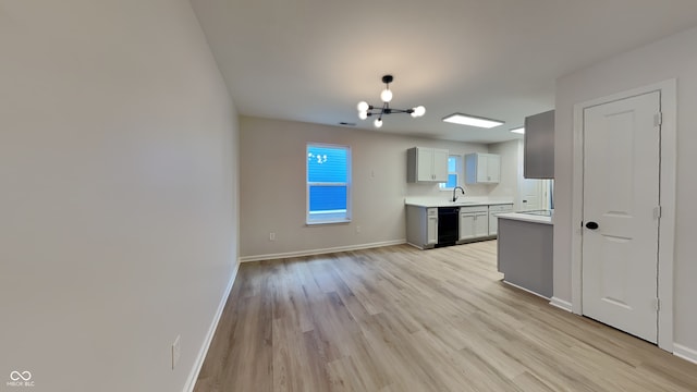 kitchen with gray cabinets, black dishwasher, sink, a notable chandelier, and light hardwood / wood-style flooring