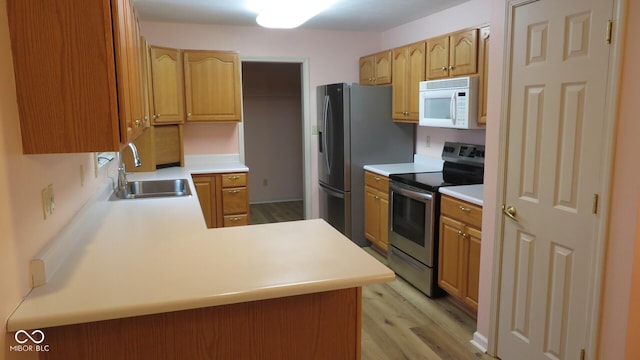 kitchen with kitchen peninsula, sink, light wood-type flooring, and stainless steel appliances