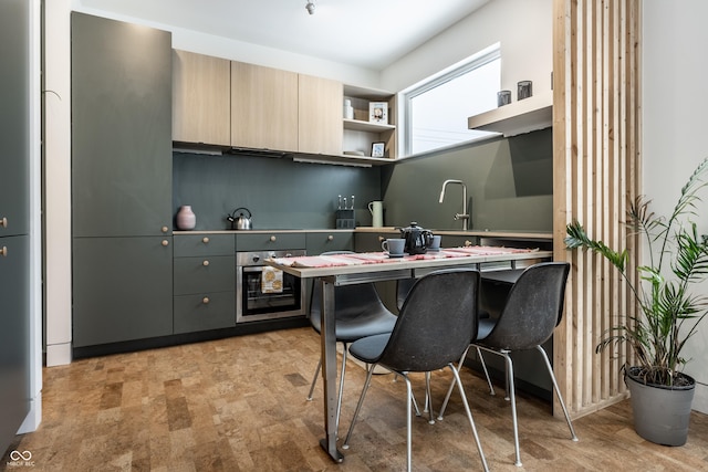 kitchen with gray cabinetry, stainless steel oven, a breakfast bar, and sink