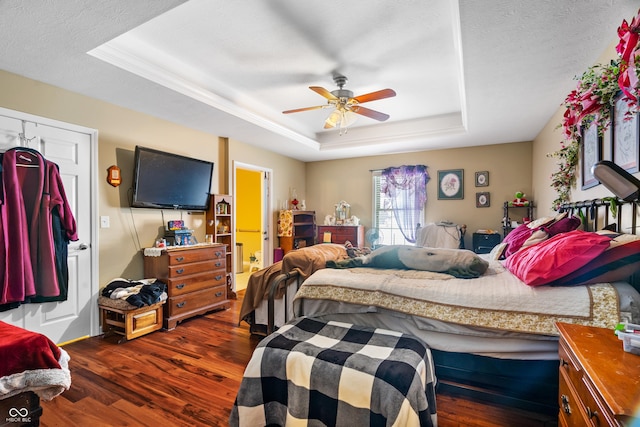 bedroom featuring a tray ceiling, dark wood-type flooring, ceiling fan, and a textured ceiling