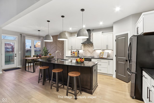 kitchen featuring sink, wall chimney range hood, hanging light fixtures, stainless steel appliances, and a center island with sink